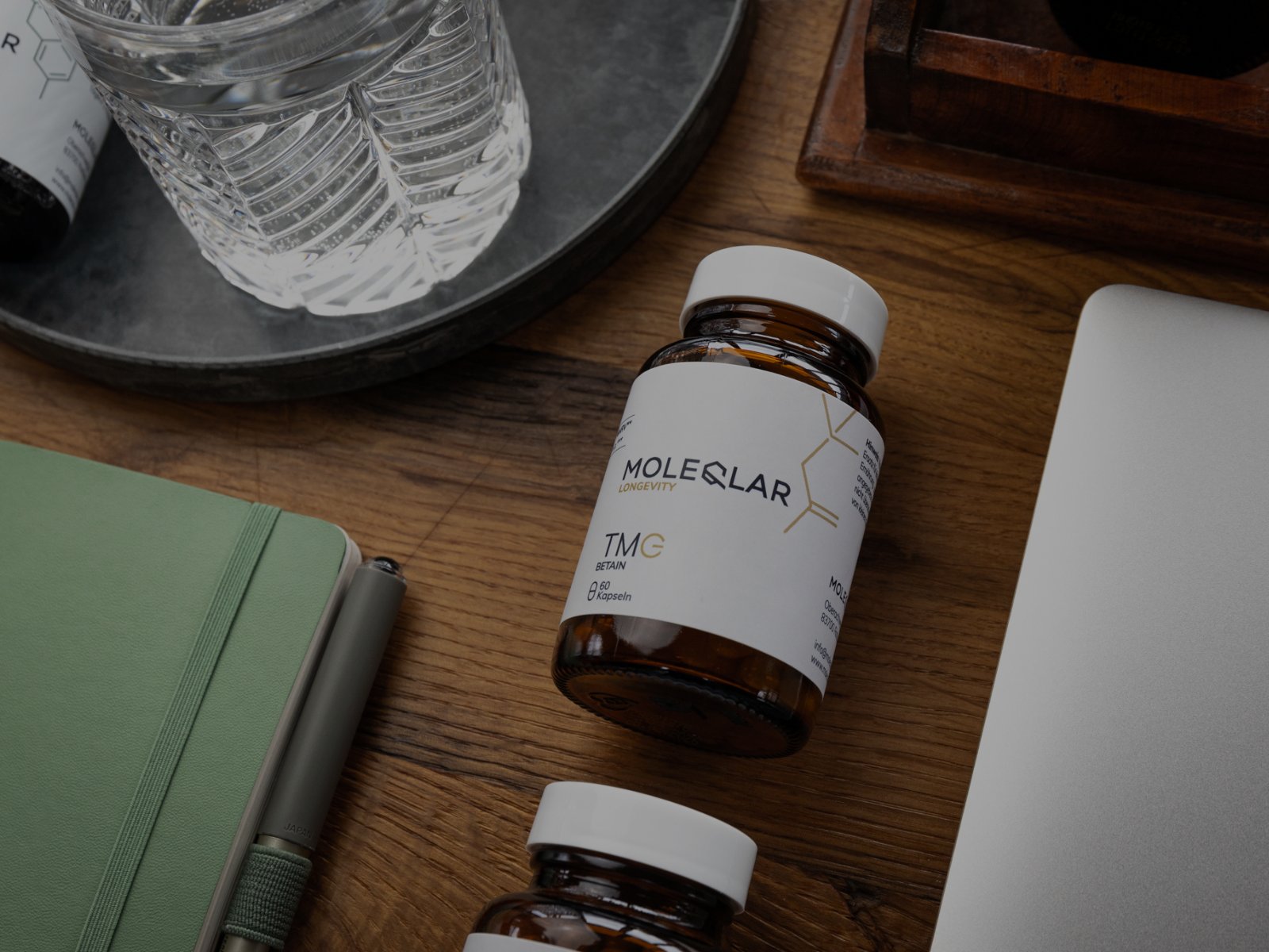 Betain (TMG) Kapseln auf einem Schreibtisch neben Laptop und Notebook.